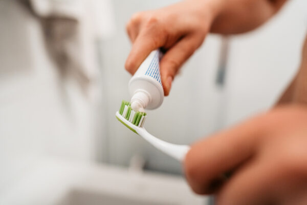 Young Man Putting On Toothpaste To Brush His Teeth In The Bathroom